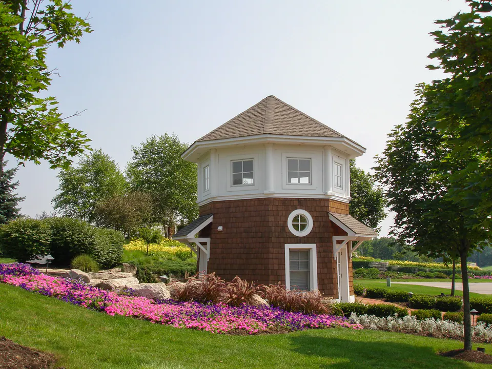 Tartan Fields entry building with sweeping pink annuals, lawn, trees, shrubs, and stone edge